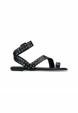 Sandalias planas negras con tiras tachonadas, que cuentan con un cierre de hebilla y punta abierta. Material suave con acabado mate y suela de goma.