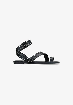 Sandalias planas negras con tiras tachonadas, que cuentan con un cierre de hebilla y punta abierta. Material suave con acabado mate y suela de goma.
