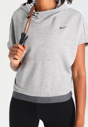 Osoba ubrana w szarą, krótkorękawową bluzę Nike z kapturem i czarne legginsy, trzymająca skakankę z czarną rączką i brązowym sznurkiem.