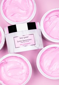 Kremete kroppsmør i en hvit krukke med marmortekstur, med et rosa lokk. Produktet har en glatt rosa konsistens, merket "Søt Granateple."