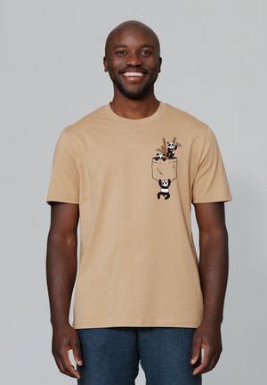 T-shirt en coton beige avec un graphique de trois pandas et des baguettes dans un design de poche. Manches courtes et col ras du cou.