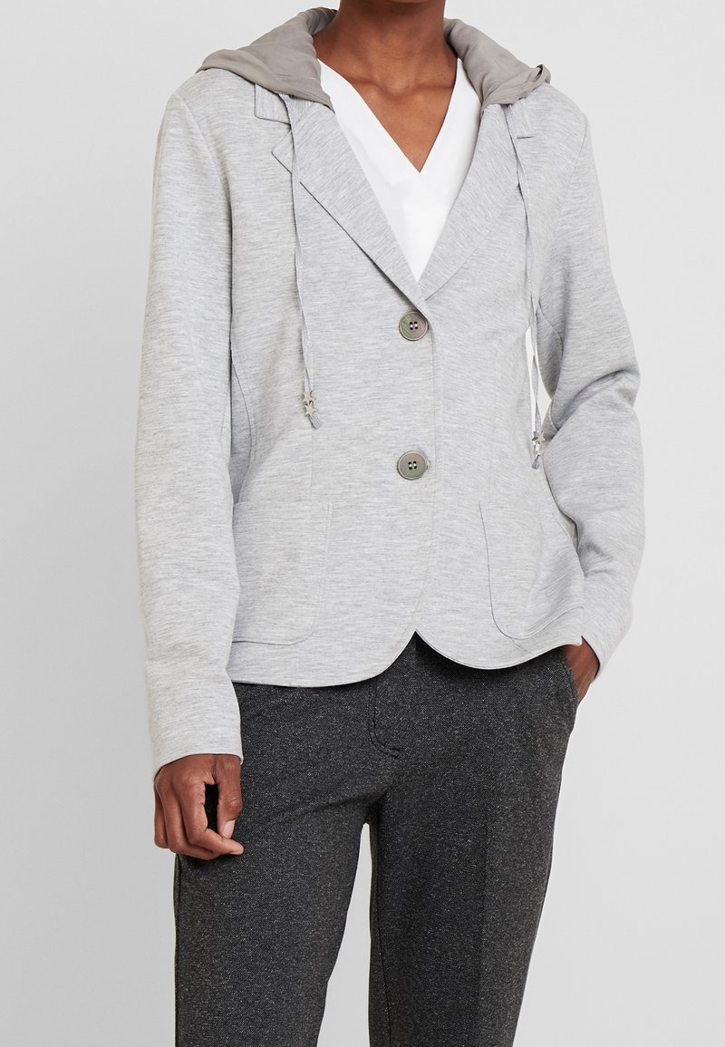 Šedé, lehké sako s kapucí; má dva knoflíky, dvě boční kapsy a šňůrky, doplněné béžovou podšívkou kapuce.