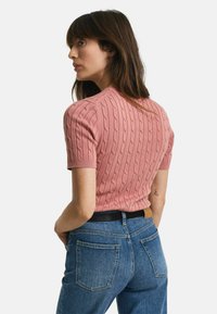 Korte mouwen, roze ribbeltrui met een textuur van kabelbreisels, gecombineerd met high-waisted blauwe jeans met achterzakken.