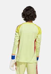 Maillot de gardien de but en jaune vif avec des accents rouges sur les côtés et des manches de poignet bleues. Manches longues avec un col rond et une texture lisse.
