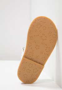 Białe sandały z teksturowaną, brązową gumową podeszwą z motywem kwiatów i liści, charakteryzujące się gładkim wykończeniem i regulowanym paskiem.