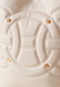 Borsa a mano in pelle crema con design trapuntato circolare, dettagli in metallo dorato e cuciture prominenti su tutta la superficie.