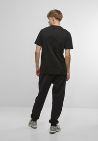 Melnas kokvilnas T-krekls ar īsām piedurknēm, apvienots ar melnajām sporta biksēm. Iezīmē brīvu piegriezumu un vienkāršu dizainu, skatīts no aizmugures.