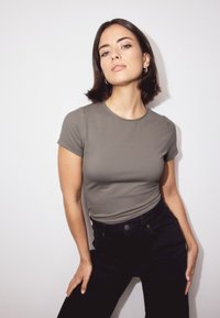 Grå kortærmet tætsiddende t-shirt kombineret med sort højtsiddende jeans, vist mod en hvid baggrund. Simpelt design og blød tekstur.