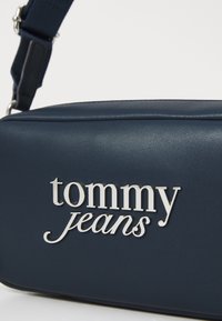Marinblåt konstläderväska med silverfärgad "tommy jeans"-logotyp. Har en rektangulär form och en avtagbar rem för bärande.