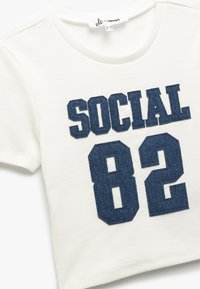 Camiseta blanca de algodón con textura acanalada que presenta letras en estilo vaquero en azul marino con la leyenda "SOCIAL 82" en un diseño atrevido y bordado.