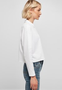 Weißes Langarm-Polohemd in lockerer Passform mit Kragen und cropped Design, kombiniert mit blauen engen Jeans.