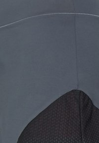 Tejido atlético gris con una superficie lisa, que presenta un panel negro texturizado en la parte inferior. Detalle de costura en contraste a lo largo de las costuras.