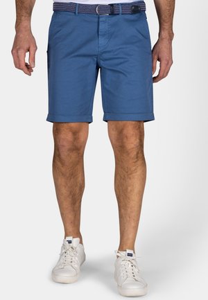 Blauwe katoenen shorts met opgerolde mouwen, vlakke voorzakken en een gemustreerde riem. G gedragen met witte sneakers en een effen wit shirt.