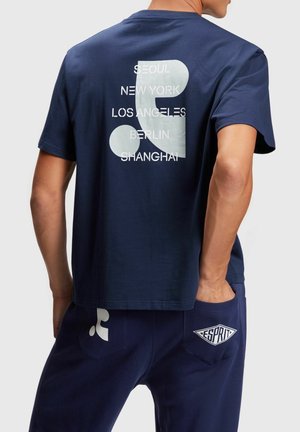 Laivastonsininen puuvillainen t-paita, jossa on selässä valkoisia kaupungin nimiä ja pyöreitä muotoja esittävä painatus. Lyhyet hihat ja rento istuvuus.