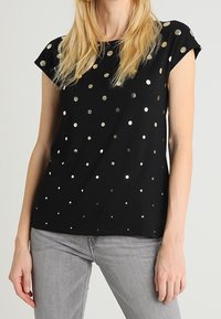 Svart kortärmad topp med silverfärgade cirkulära paljetter i olika storlekar, med avslappnad passform och mjuk tyger.