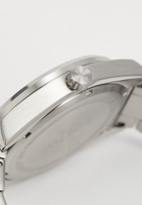 Montre en acier inoxydable argenté avec un design épuré, une lunette texturée et une couronne proéminente marquée "Hugo". Fini brossé lisse.