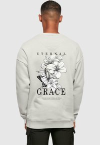 Lys grå sweatshirt med et blomster- og sommerfugldesign i sort, hvor ordene "ETERNAL GRACE" står klart frem.