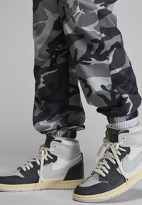Svarta och grå kamouflagebyxor med elastiska muddar, kombinerat med hög-top sneakers med svart, vitt och krämfärgat läder samt snören.