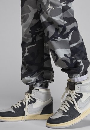 Svarta och grå kamouflagebyxor med elastiska muddar, kombinerat med hög-top sneakers med svart, vitt och krämfärgat läder samt snören.