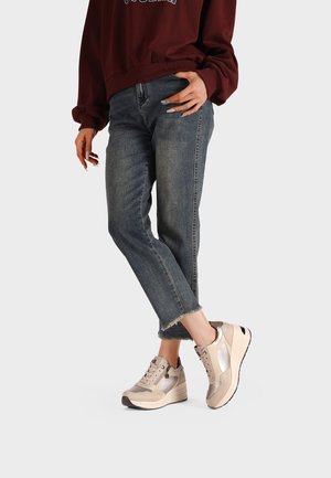 Sneakers beige con una finitura testurizzata, dotati di una suola a zeppa, lacci e accenti metallici, abbinati a jeans in denim a vita alta.