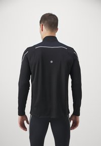 Czarna koszulka sportowa z długim rękawem, z refleksyjnymi akcentami i okrągłym detalem z tyłu, zaprojektowana z myślą o wydajności i ruchu.