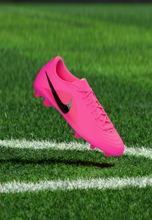 Gheată de fotbal roz aprins cu logo negru Nike plutind deasupra ierbii, aproape de liniile albe de delimitare a terenului.