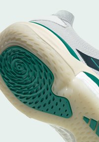 Gros plan de la semelle blanche d'une chaussure de sport avec motif d'adhérence en caoutchouc vert et une semelle intermédiaire beige texturée pour l'accroche et le maintien.