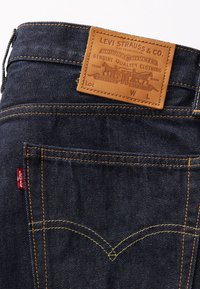 Jeans de mezclilla azul oscuro con una etiqueta de cuero marrón en la parte posterior, con costuras amarillas y una pequeña etiqueta roja de Levi's en un costado.
