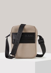 Borsa a tracolla in nylon beige con tracolla nera e logo, dotata di una tasca frontale con zip e forma rettangolare. Texture liscia.