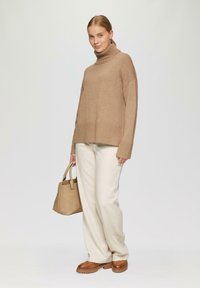 Beige coltrui met geribbelde zoom, gecombineerd met crèmekleurige wijde broek en bruine platform schoenen. Lichtbruine handtas met handvat.