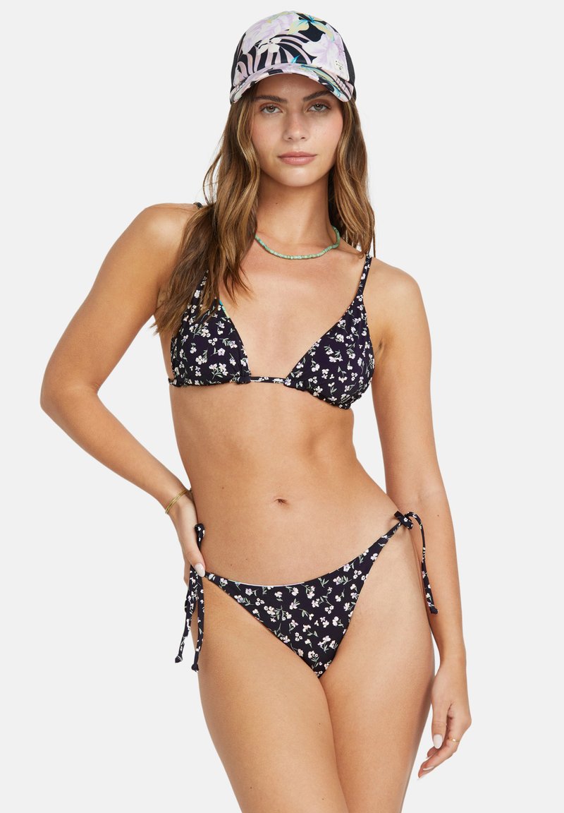 Črni cvetlični bikini s trikotno zgornjim delom in spodnjim delom s stranskimi vezavami. Manekenka nosi kapico s potiskom in ogrlico, ki ima gladko teksturo tkanine.