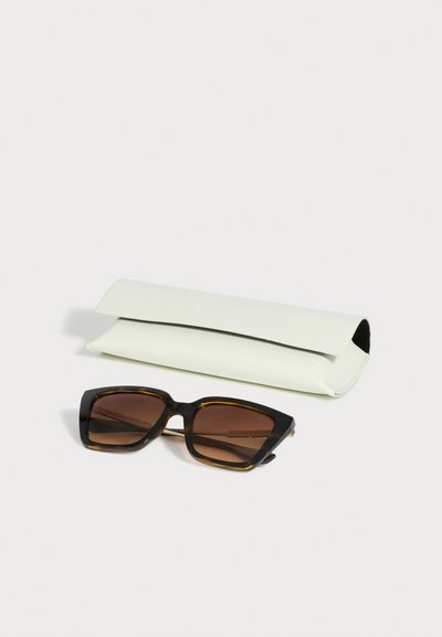 Lunettes de soleil rectangulaires en écaille avec verres marron, placées devant un étui souple blanc pliable sur fond clair.