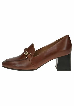 Chaussure en cuir brun avec un bout arrondi, dotée d'une sangle décorative et d'éléments en métal doré. Talon carré avec une texture nervurée.