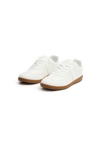 Zapatillas blancas hechas de material sintético con suela de goma texturizada. Incluyen características como puntera redonda, cordones y dos franjas laterales.