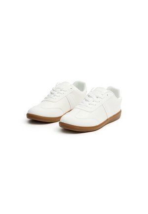 Zapatillas blancas hechas de material sintético con suela de goma texturizada. Incluyen características como puntera redonda, cordones y dos franjas laterales.