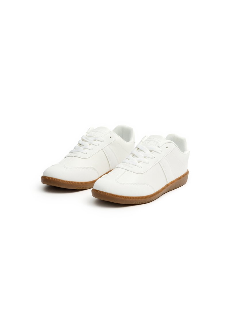 Zapatillas blancas hechas de material sintético con suela de goma texturizada. Incluyen características como puntera redonda, cordones y dos franjas laterales.