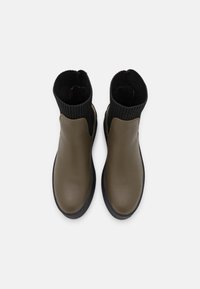 Olive green ankle boots with a smooth leather upper and black ribbed fabric sock-like collar. Rubber sole for grip and durability.