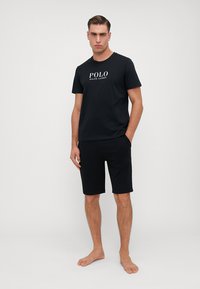 Tricou negru din bumbac cu logo-ul "POLO RALPH LAUREN", combinat cu pantaloni scurți negri. Design simplu, mâneci scurte, croială lejeră și fără modele.
