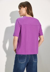 Haut violet à manches courtes avec un col rond, coupe décontractée et texture lisse ; associé à un jean en denim bleu.
