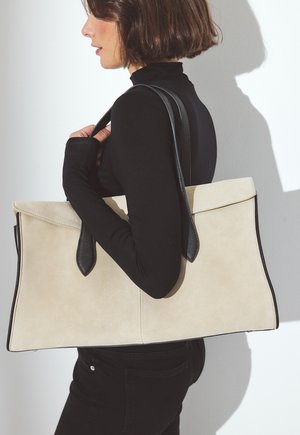 Borsa tote in suede beige con dettagli in pelle nera, forma rettangolare e doppio manico, caratterizzata da una texture liscia e un design elegante.