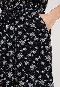 Zwarte shorts met een wit palmbomenpatroon, elastische tailleband, trekkoord met groene accenten en zijzakdetail.