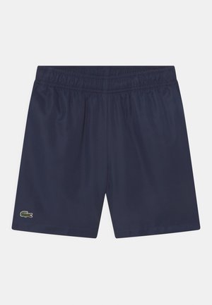 Pantalones cortos deportivos azul marino con cintura elástica y pequeño logo verde de cocodrilo en el dobladillo de la pierna izquierda, exhibidos sobre fondo blanco.