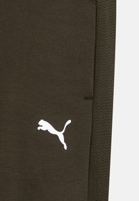 Olivza zaļas sporta bikses ar gludu tekstūru un baltu PUMA logo, ar šauru piegriezumu un adītu jostasvietu.