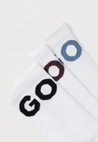 Bavlnené ponožky v bielej farbe majú vyšívaný nápis "GO" v čiernej, modrej a bordovej farbe. Dizajn obsahuje rebrovanú textúru na vrchu.