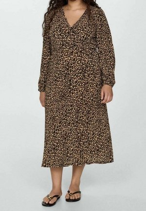 Femme portant une robe midi à manches longues, col en V, imprimé léopard, avec des sandales plates noires ornées d'une boucle dorée.