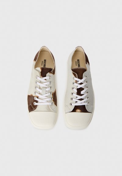 Sneakers med en blandning av beige och brun koshudsmönster, vita snörningar och en krämfärgad gummitå. Platt, avslappnad design med rund form.