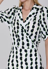 Robe blanche avec un imprimé de feuilles noires et vertes, avec un design enroulé et des manches courtes bouffantes, fabriquée en tissu léger.