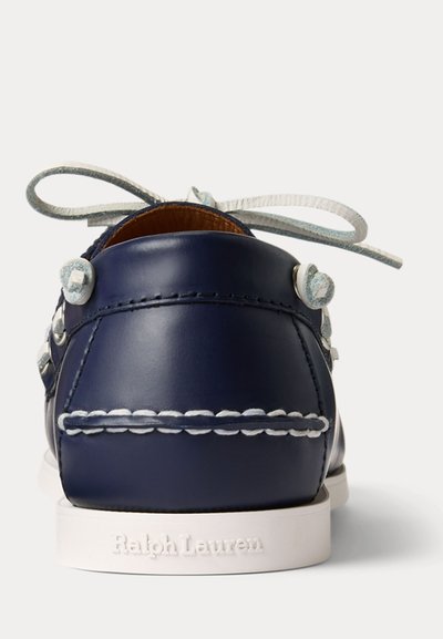 Scarpa da barca in pelle blu navy con cuciture bianche, lacci bianchi annodati e suola bianca con marchio "Ralph Lauren" vista dal tallone.