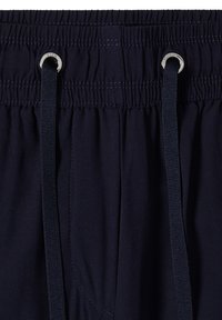 Ceinture élastique marine avec cordons passés à travers des œillets métalliques sur un tissu foncé, montrant les détails de la couture et la texture.