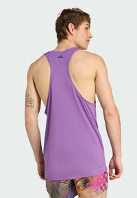Lilla tanktop med racerback-design, lavet af letvægtsmateriale. Har Adidas-logoet på den øverste ryg.